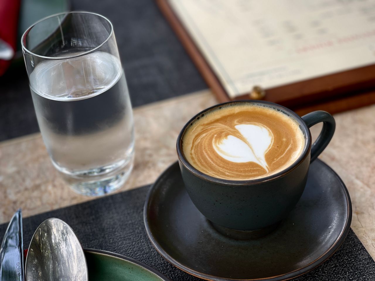 The Art of Drawing Readers In: Your attractive post title goes here Close-up of a latte with heart-shaped latte art beside a glass of water on a cafe table.